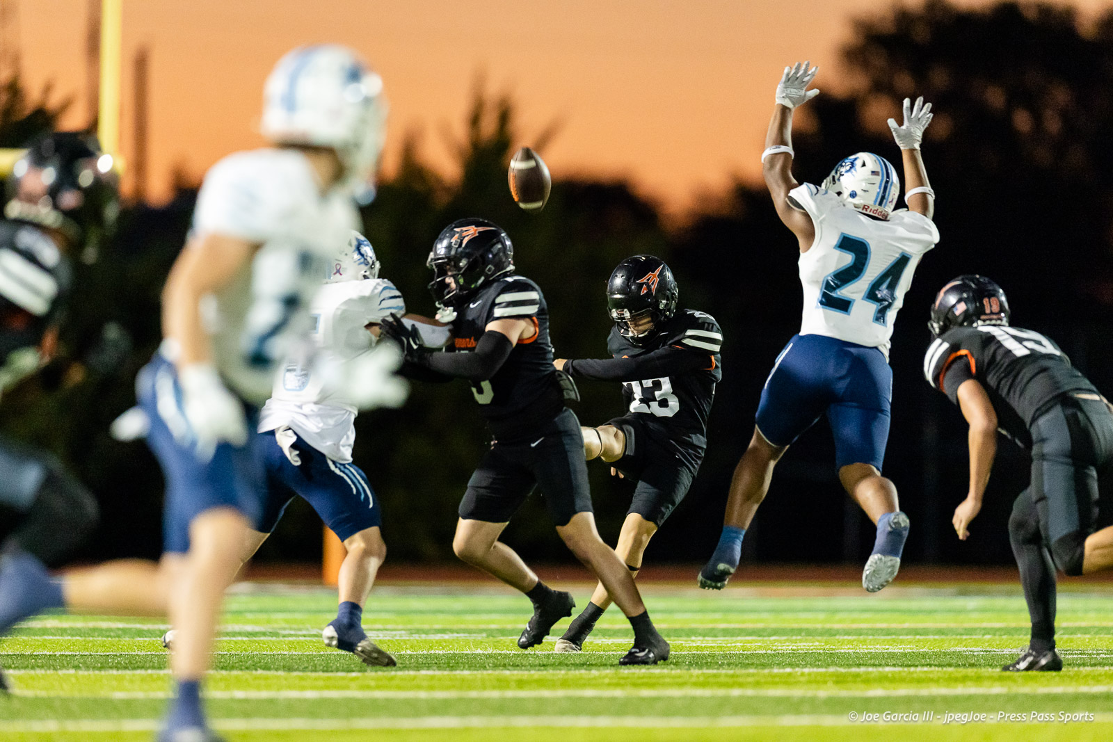 west-plains-vs-dumas-football-jpegJoe-pps-23 | Press Pass Sports Football players in white and black uniforms reach for an airborne ball during a night game on a green turf field.