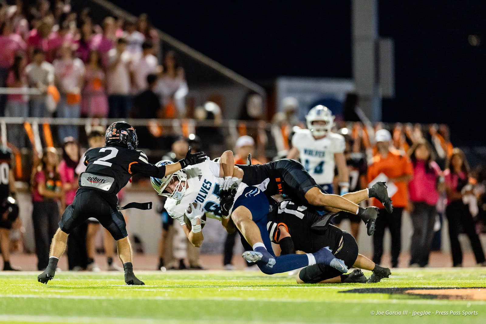 west-plains-vs-dumas-football-jpegJoe-pps-25 | Press Pass Sports Two football players collide as a ball carrier in white jersey is tackled by a defender in black, mid-air on a bright field with a cheering crowd behind.