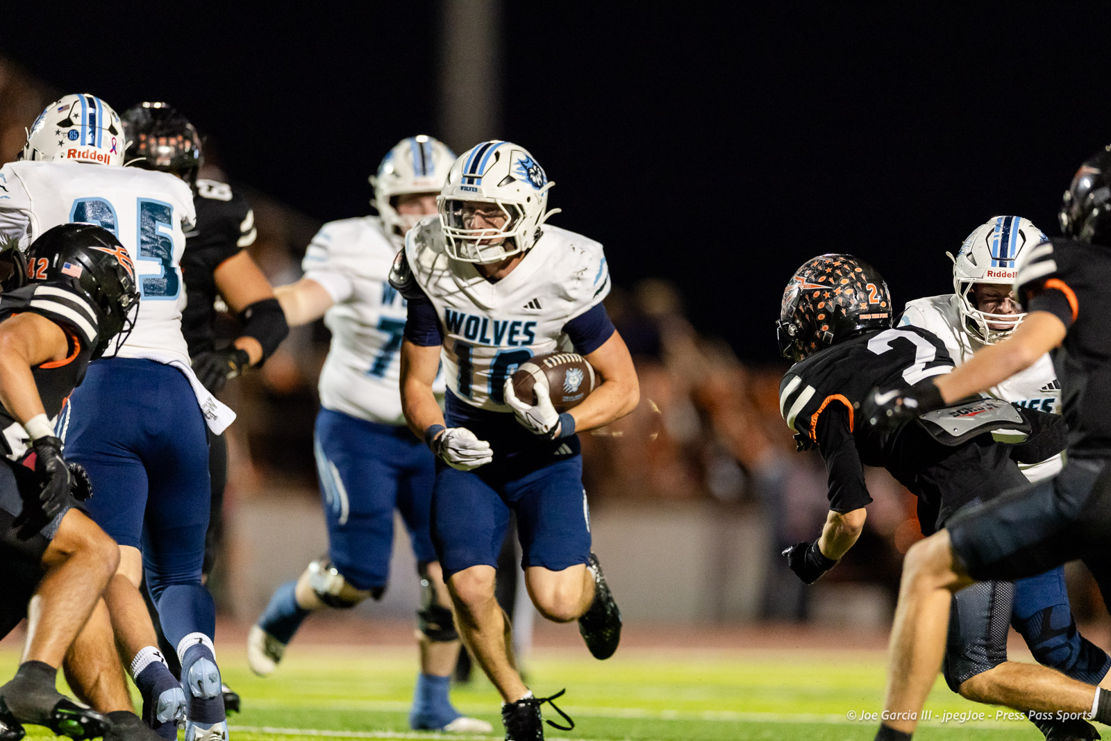 west-plains-vs-dumas-football-jpegJoe-pps-26 | Press Pass Sports Wolves running back in white and blue jersey with ball, sprinting through defenders at night.