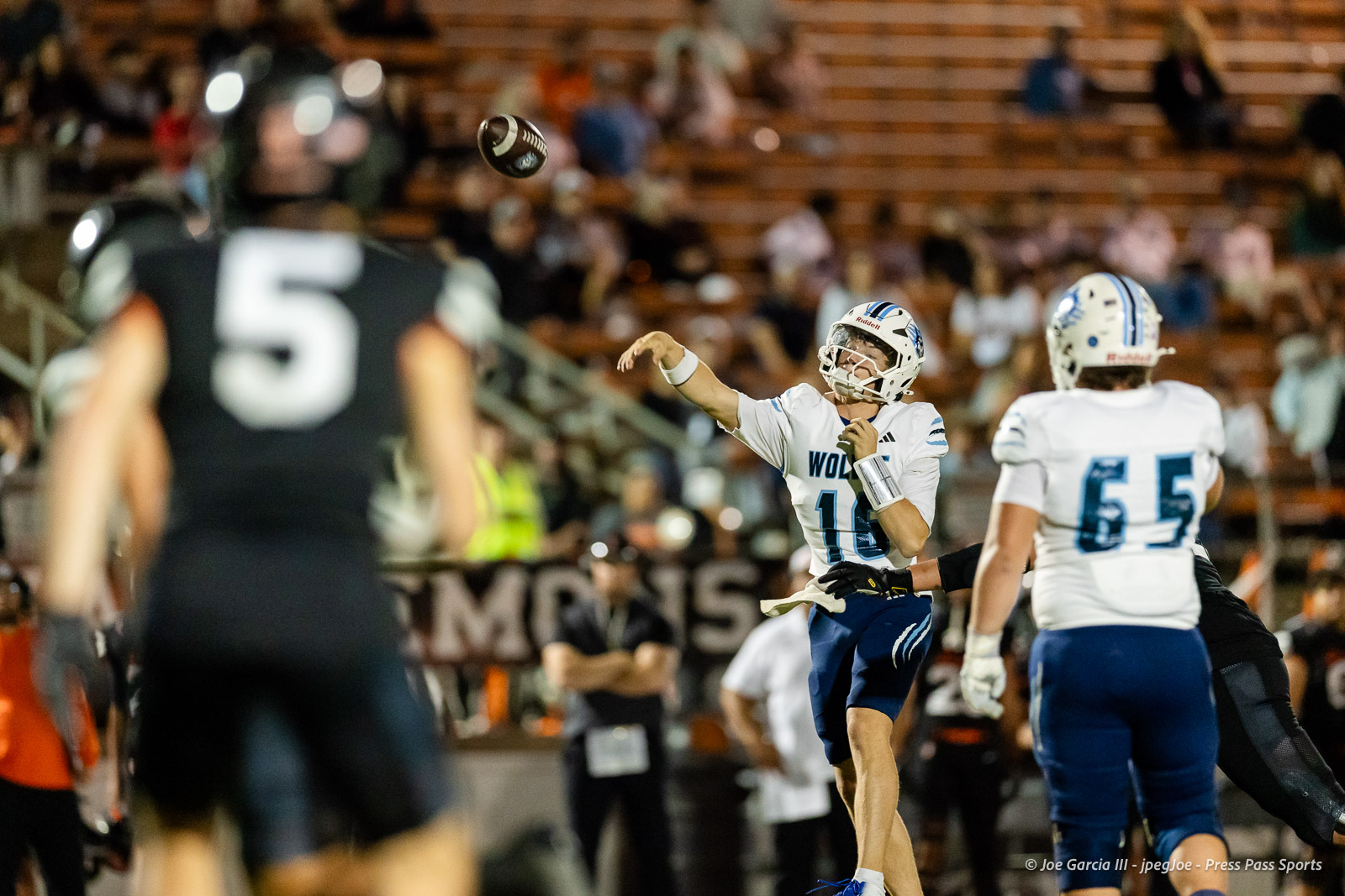 west-plains-vs-dumas-football-jpegJoe-pps-28 | Press Pass Sports Quarterback in white and blue prepares to throw a football as teammates and defenders close in on a crowded sideline.