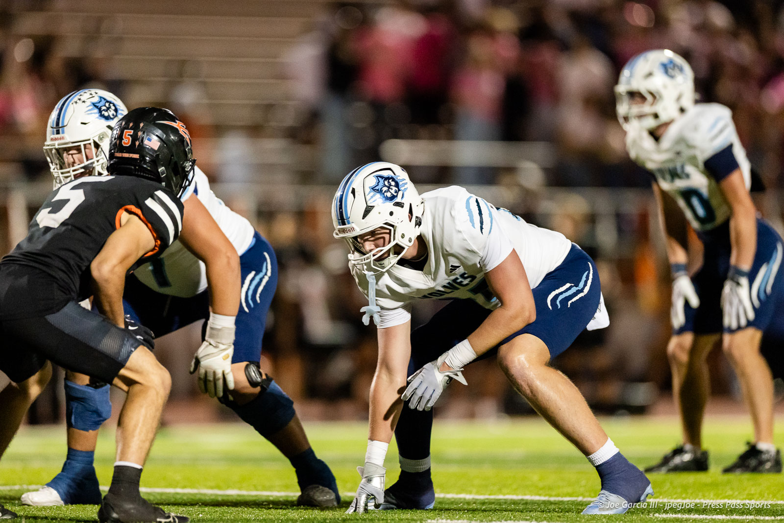 west-plains-vs-dumas-football-jpegJoe-pps-29 | Press Pass Sports American football players line up at the line of scrimmage; a white-team center crouches ready to snap the ball while teammates guard him.