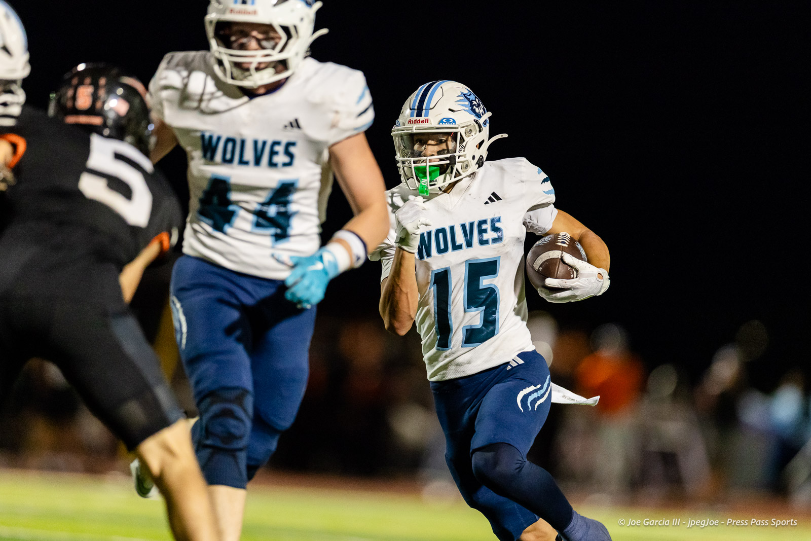 west-plains-vs-dumas-football-jpegJoe-pps-30 | Press Pass Sports Football player in a white Wolves jersey with number 15 carrying the ball during a night game under stadium lights.