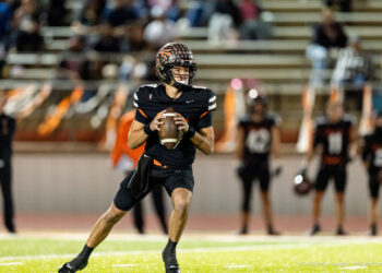 west-plains-vs-dumas-football-jpegJoe-pps-36 | Press Pass Sports Quarterback in a black uniform runs with the football, looking downfield during a game on a lit field.