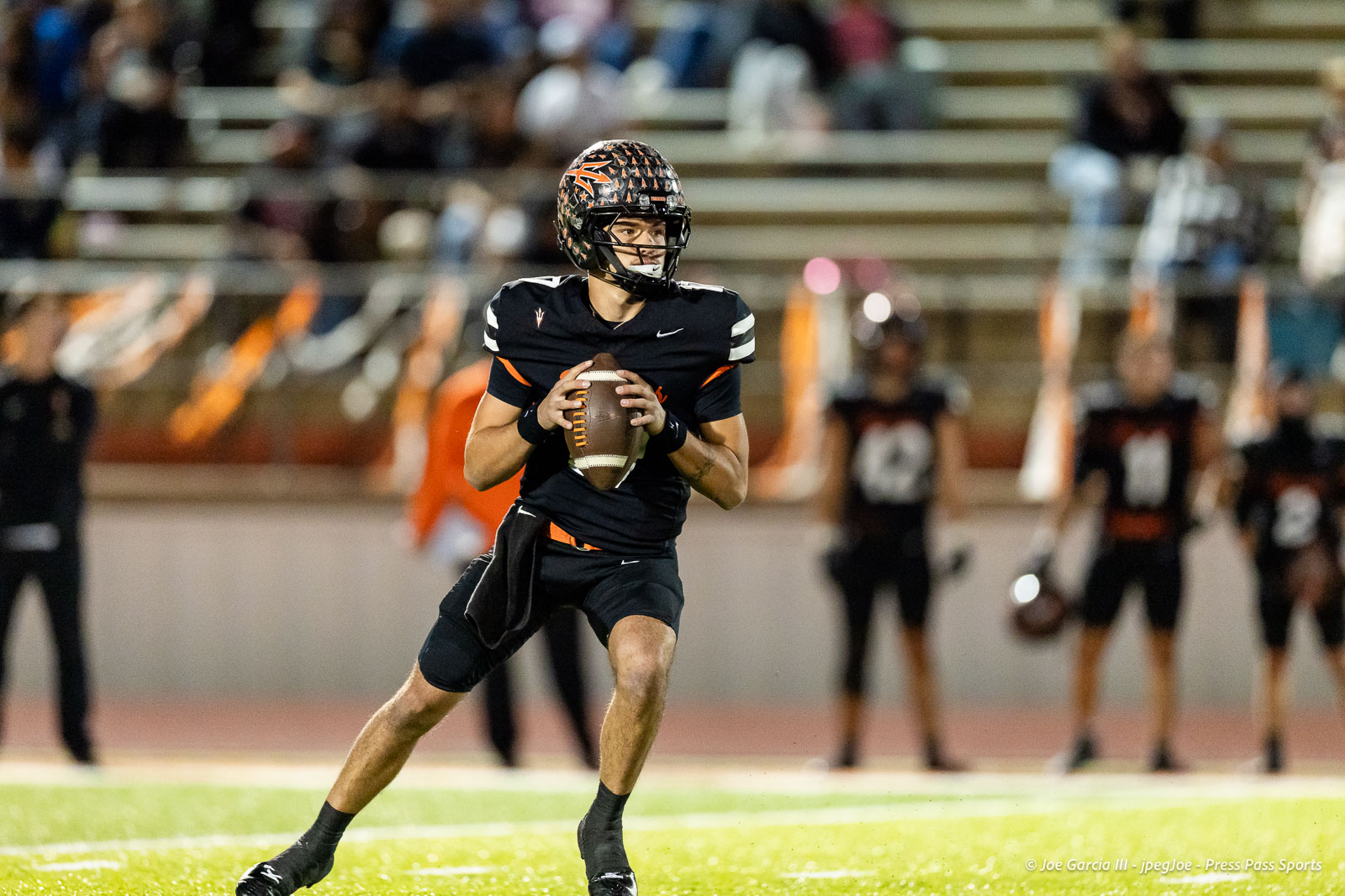 west-plains-vs-dumas-football-jpegJoe-pps-36 | Press Pass Sports Quarterback in a black uniform runs with the football, looking downfield during a game on a lit field.