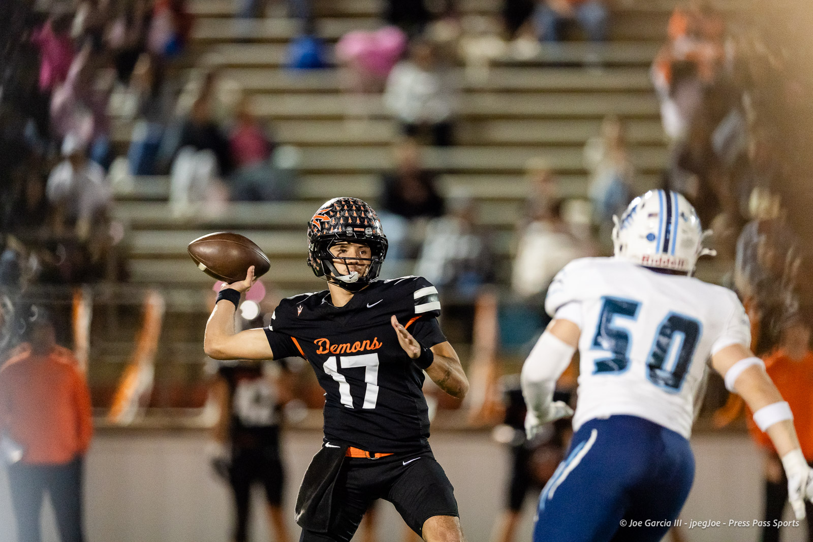 west-plains-vs-dumas-football-jpegJoe-pps-37 | Press Pass Sports Male football quarterback in black Demons jersey (number 11) throwing a pass on the field with a defender in white nearby.