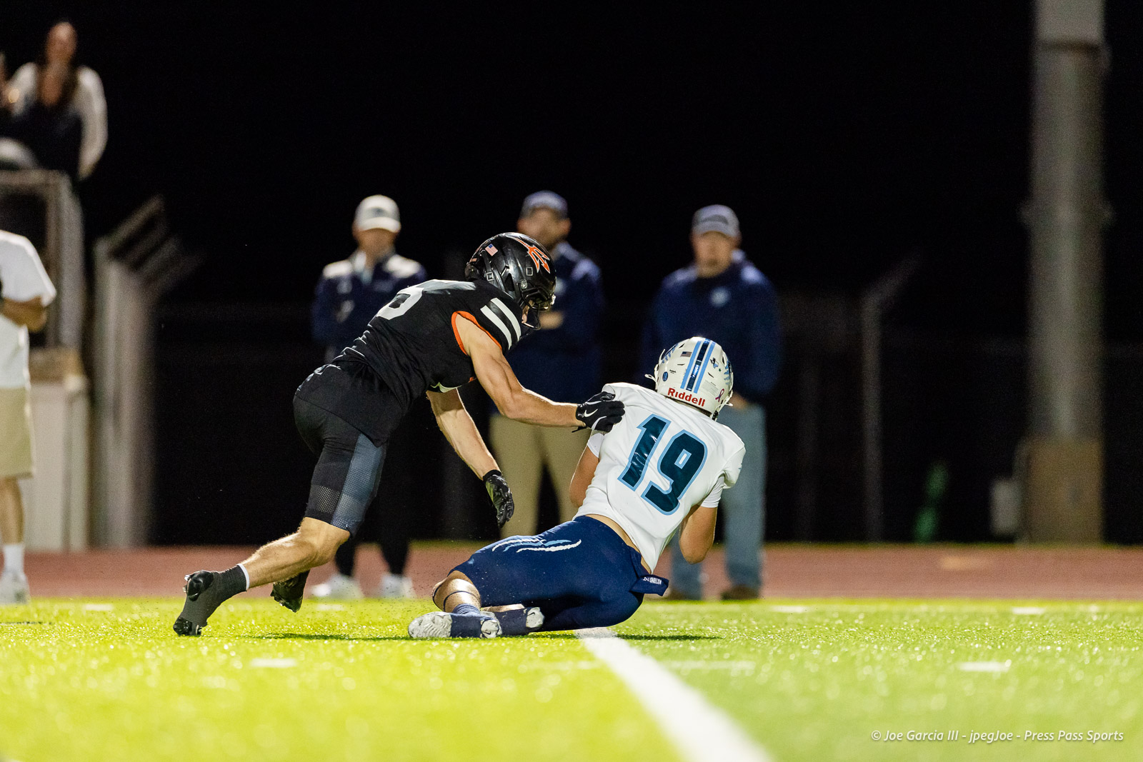 west-plains-vs-dumas-football-jpegJoe-pps-40 | Press Pass Sports Two football players collide on a brightly lit turf field at night; one in a black uniform reaches toward the opponent in a white jersey with number 19.