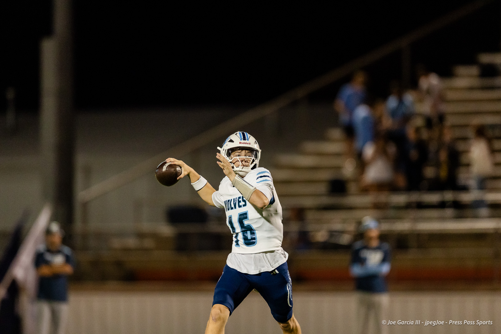 west-plains-vs-dumas-football-jpegJoe-pps-43 | Press Pass Sports Quarterback in white jersey number 15 throws a pass during a night football game, stadium stands blurred in the background