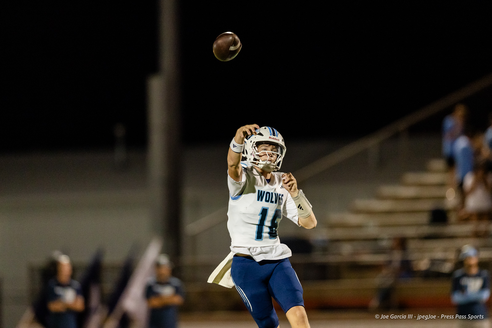 west-plains-vs-dumas-football-jpegJoe-pps-44 | Press Pass Sports Quarterback in a white Wolves uniform throws a pass at night, ball mid-air, stadium lights in the background