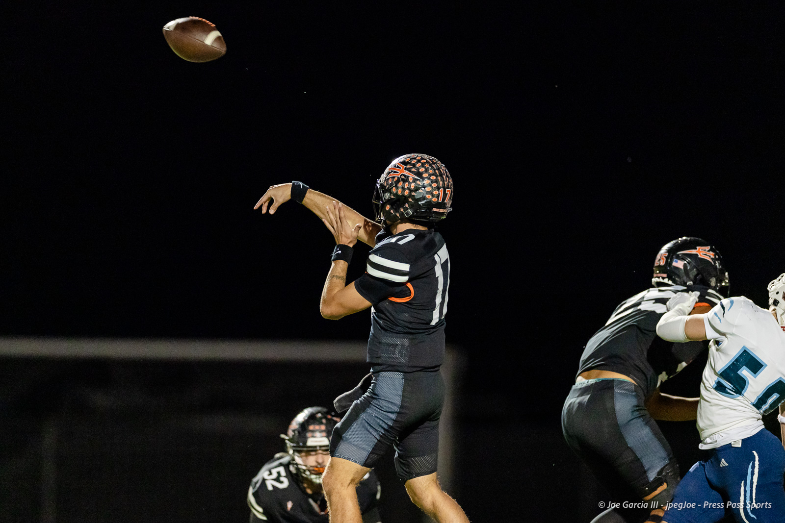 west-plains-vs-dumas-football-jpegJoe-pps-47 | Press Pass Sports A football quarterback in a dark jersey throws a pass while teammates and opponents collide in the background at night.