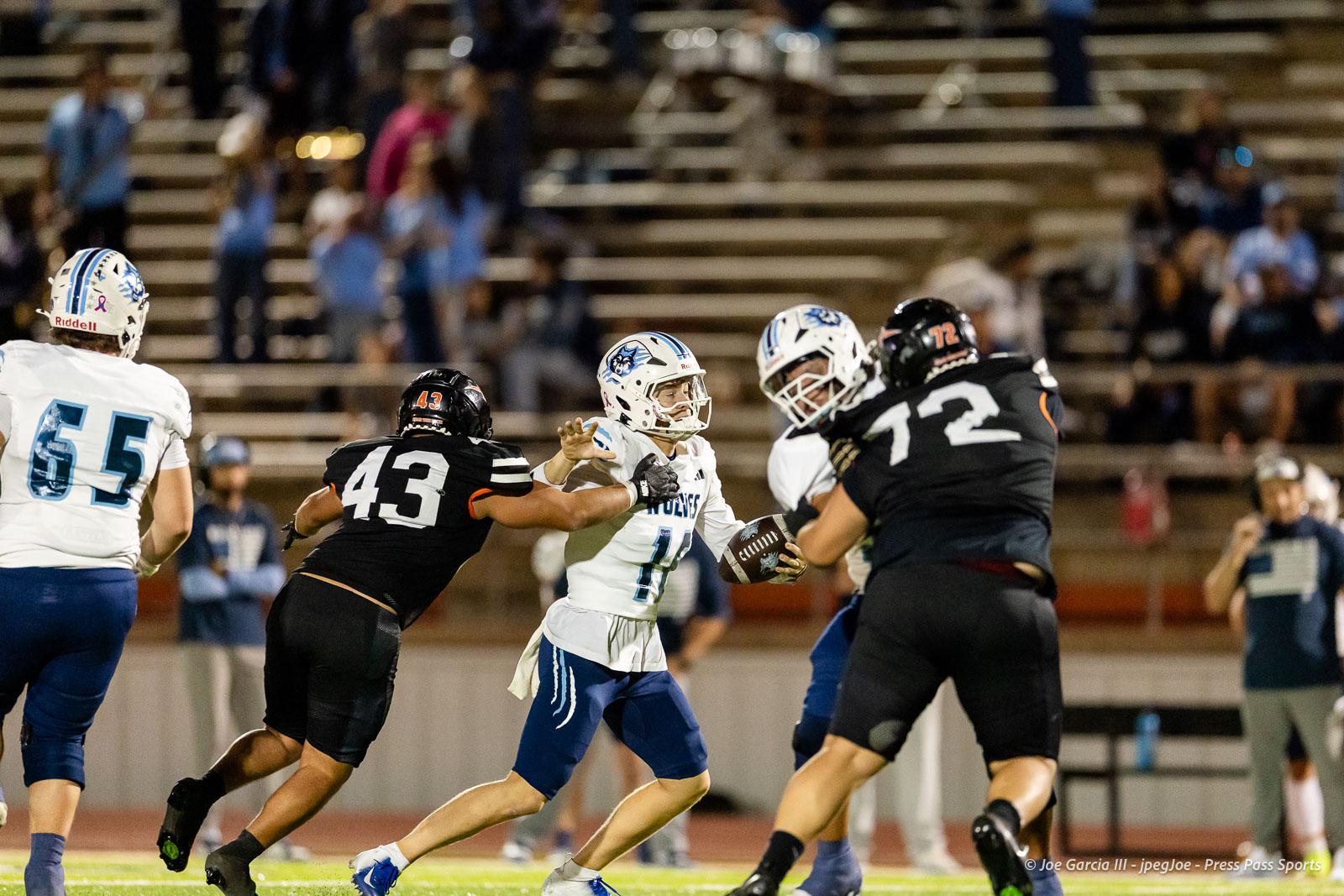 west-plains-vs-dumas-football-jpegJoe-pps-50 | Press Pass Sports Night-time football play: white team QB (number 11) with the ball, fending off a tackle from black team (number 43) as another black defender (number 72) closes in.