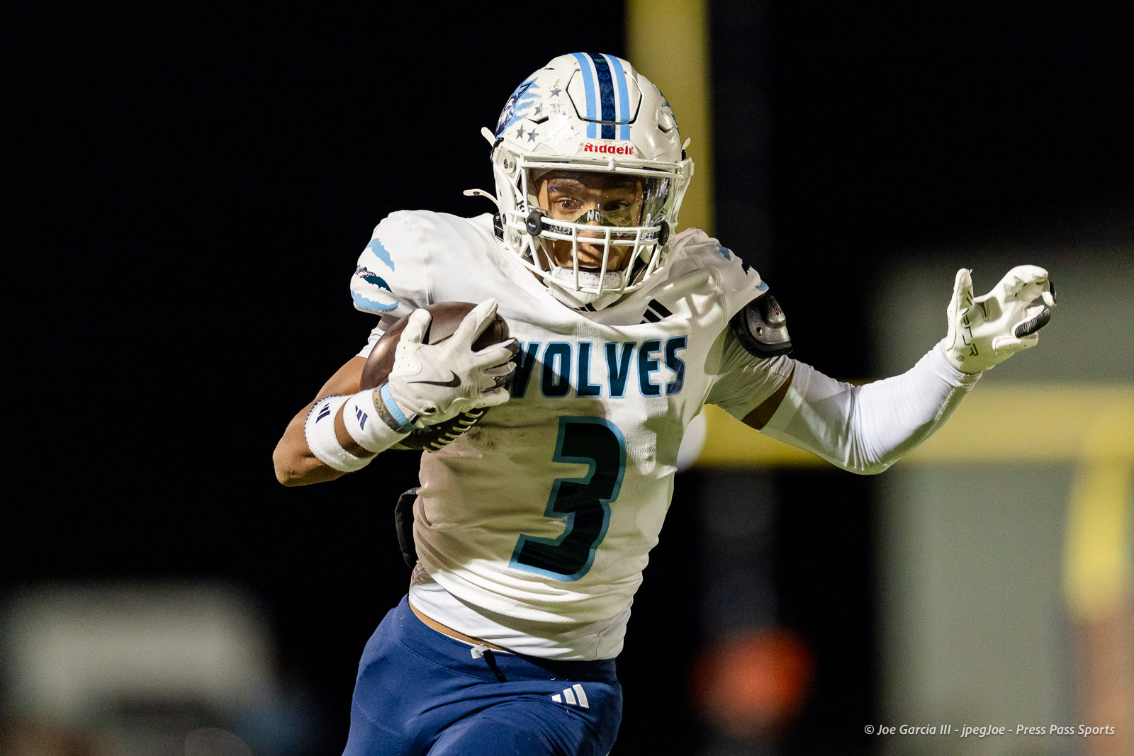 west-plains-vs-dumas-football-jpegJoe-pps-53 | Press Pass Sports American football player in a white Wolves jersey with number 3 running with the ball at night, wearing a helmet and protective gear on a dark field.