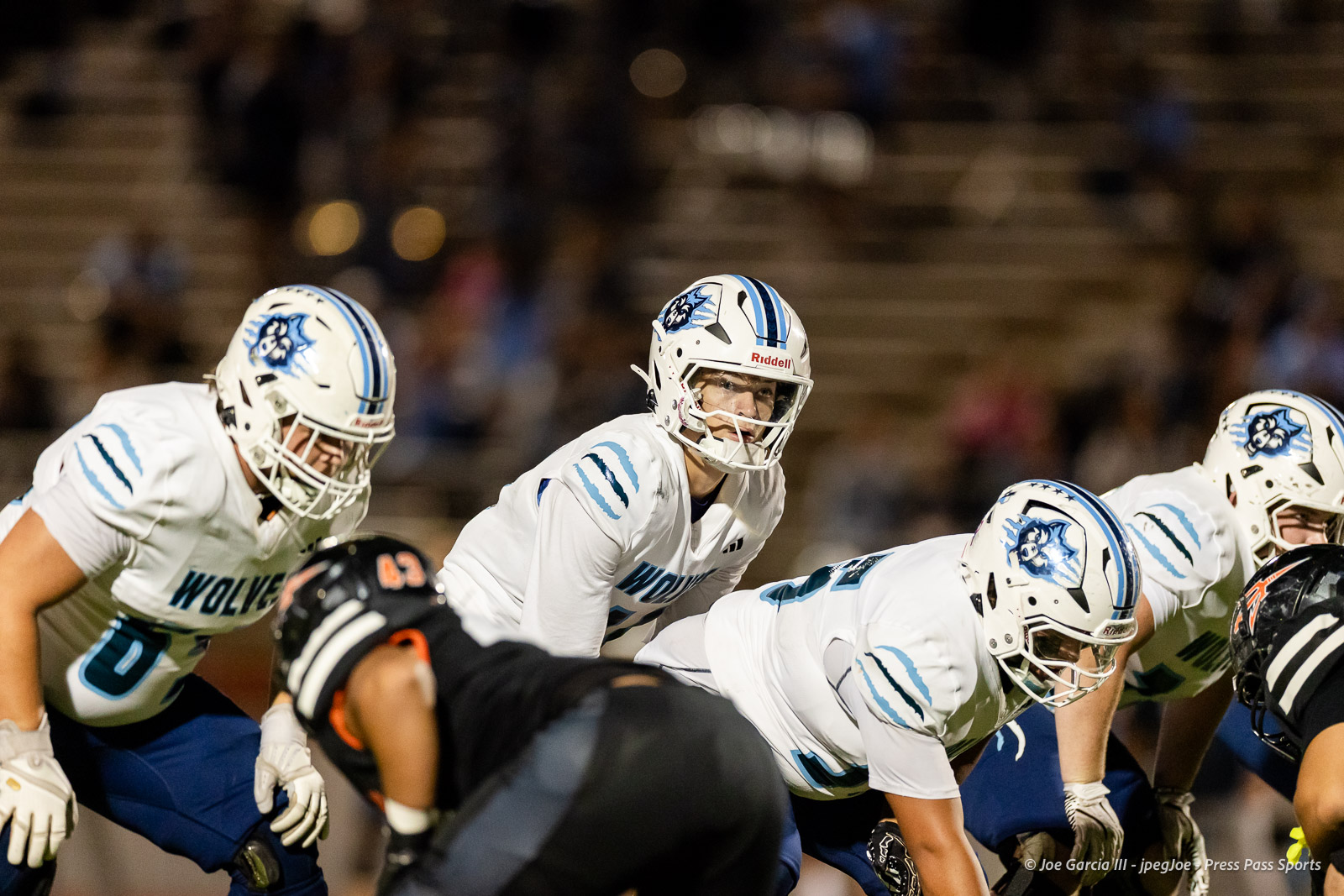 west-plains-vs-dumas-football-jpegJoe-pps-54 | Press Pass Sports Football players in white Wolverines uniforms line up at the line of scrimmage during a game at night.