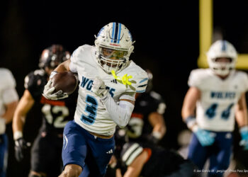 west-plains-vs-dumas-football-jpegJoe-pps-68 | Press Pass Sports Football player in white and blue uniform (#3) carries the ball and runs under stadium lights in a night game.