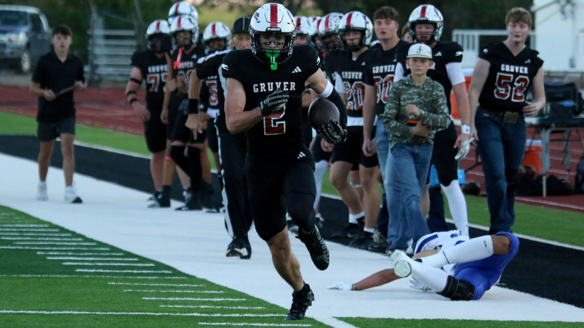 Stratford vs Gruver - Mason Lankford | Press Pass Sports Gruver football player with number 2 runs with the ball along the sideline, teammates in pursuit behind him, on a football field.