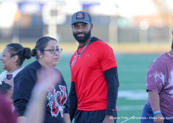 IMG_2467 | Press Pass Sports Bearded man in a red athletic shirt and cap among a group on a sports field.