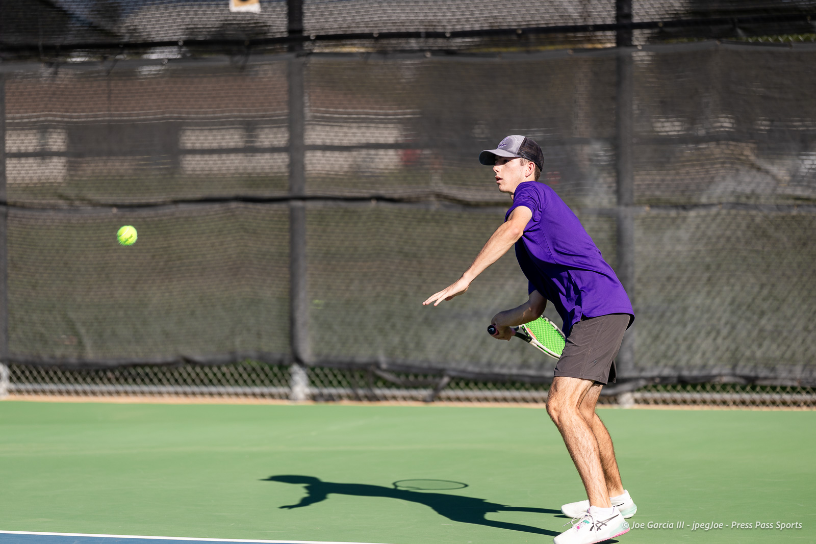 canyon-regional-tennis-9 | Press Pass Sports Tennis player in a purple shirt and cap preparing to hit a forehand on a green court, ball approaching from the left.