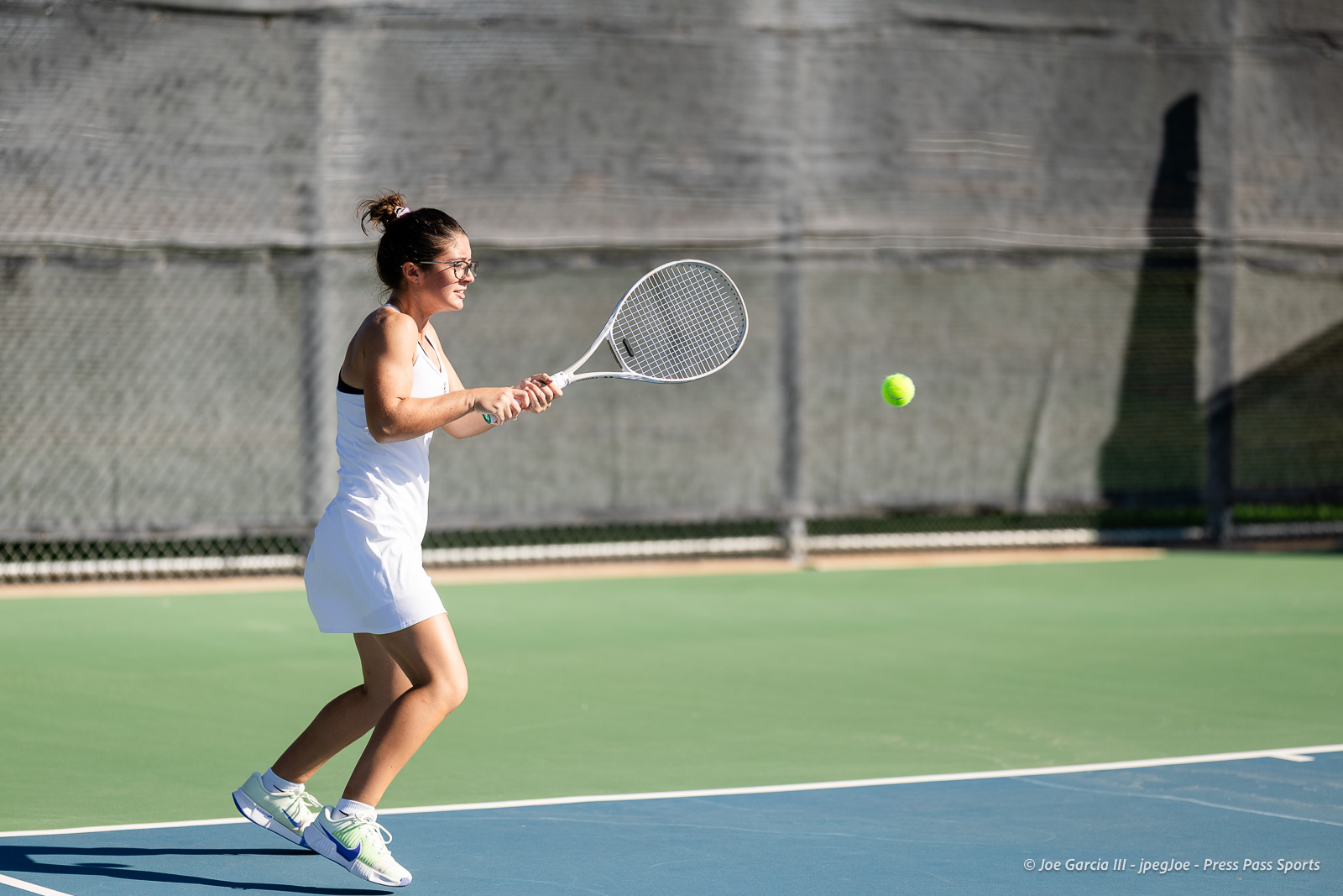 canyon-regional-tennis-13 | Press Pass Sports Female tennis player in a white outfit hits a ball with a racket on an outdoor court.