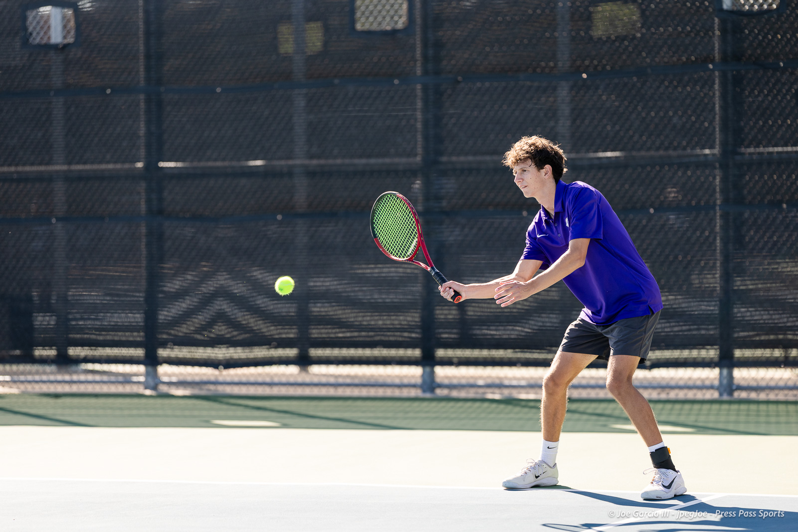 canyon-regional-tennis-20 | Press Pass Sports Tennis player in a purple shirt preparing to hit a backhand volley on an outdoor court as a bright tennis ball approaches.