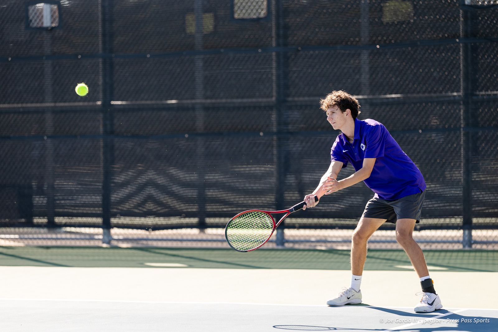 canyon-regional-tennis-21 | Press Pass Sports Tennis player in a purple shirt and gray shorts preparing to hit a forehand on an outdoor court with a green ball in the air nearby.