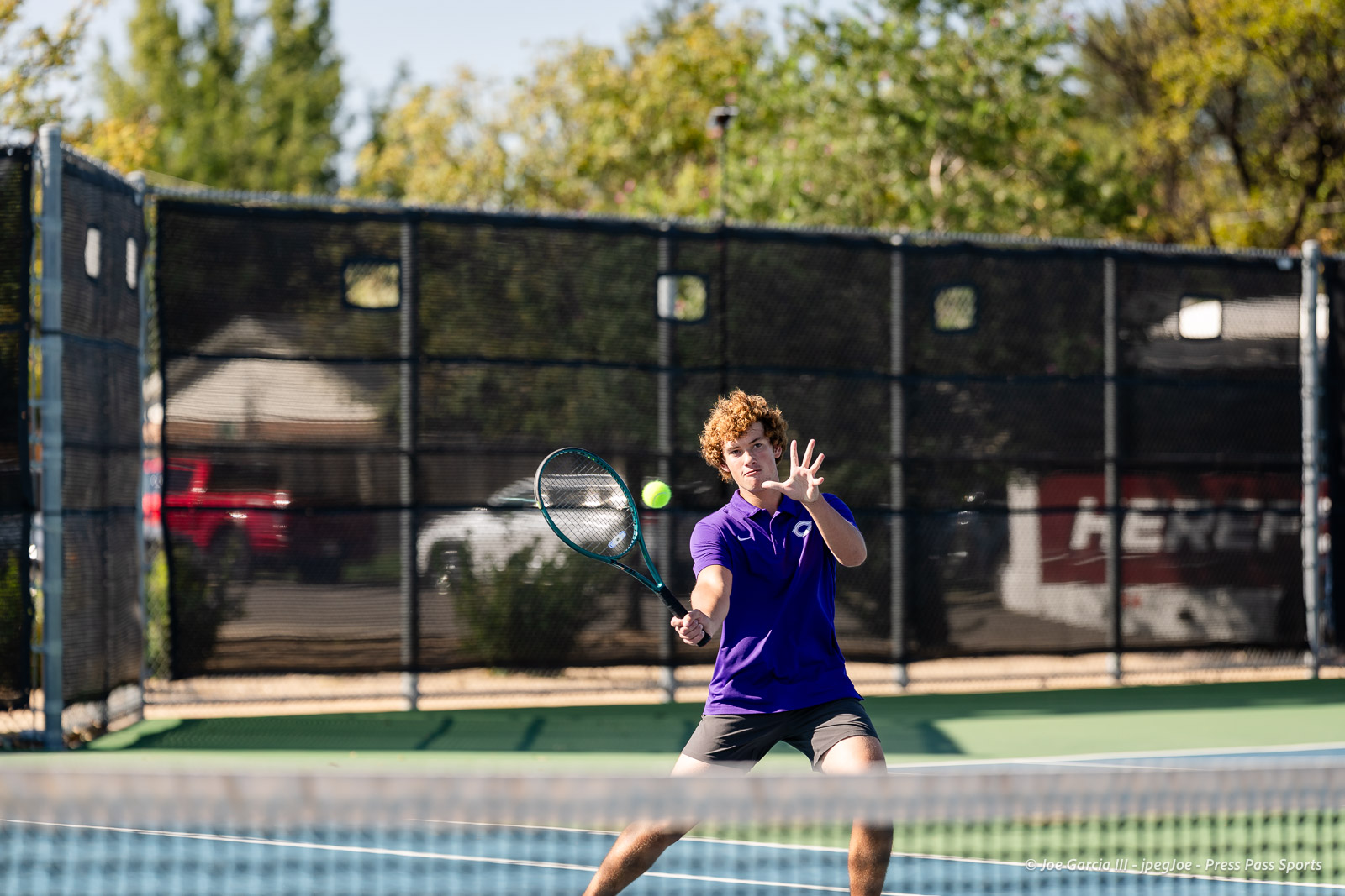 canyon-regional-tennis-28 | Press Pass Sports Tennis player in a purple shirt preparing to hit a ball on an outdoor court with a chain-link fence in the background around.