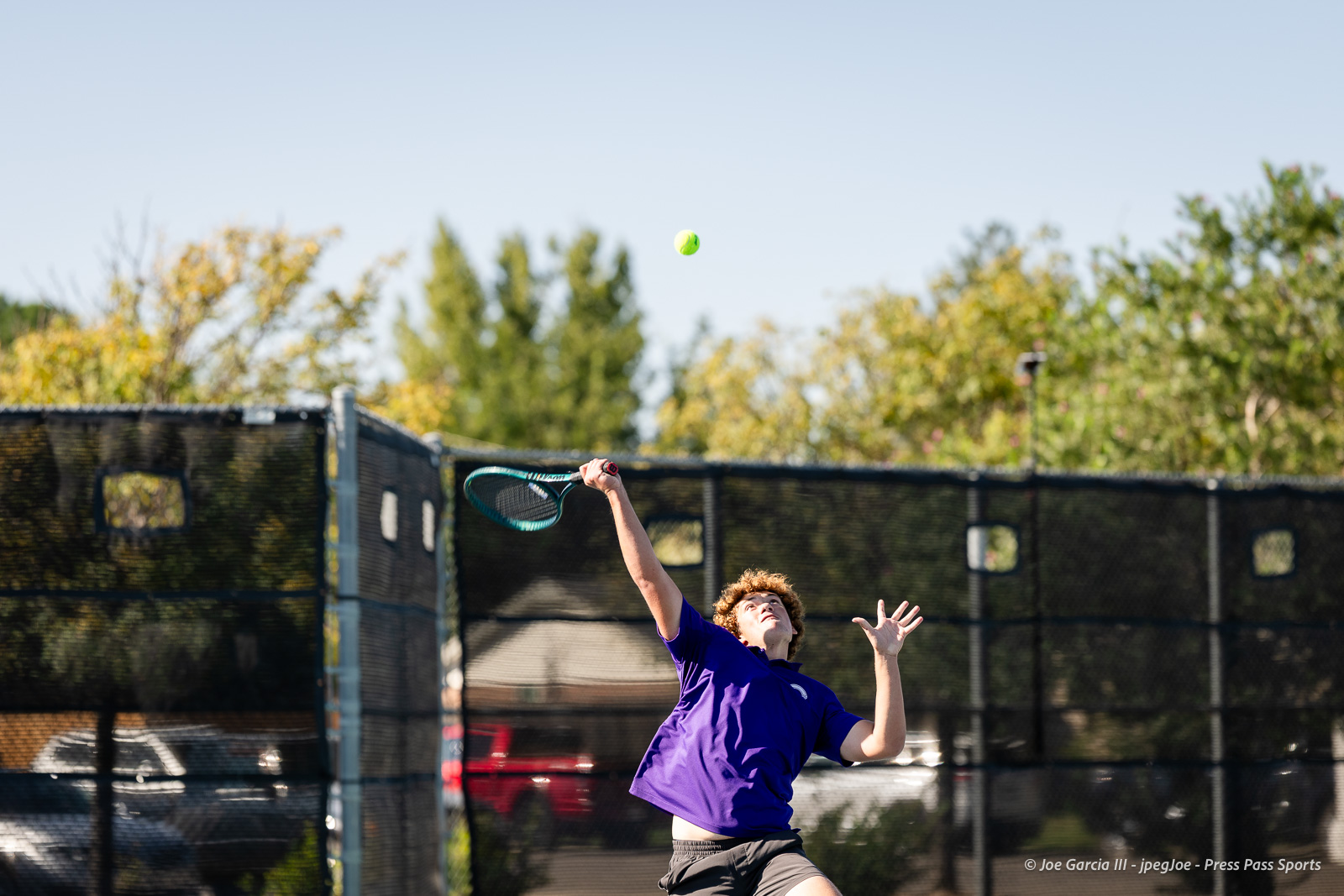 canyon-regional-tennis-30 | Press Pass Sports Young tennis player in a purple shirt serving on an outdoor court with a yellow ball mid-air above him