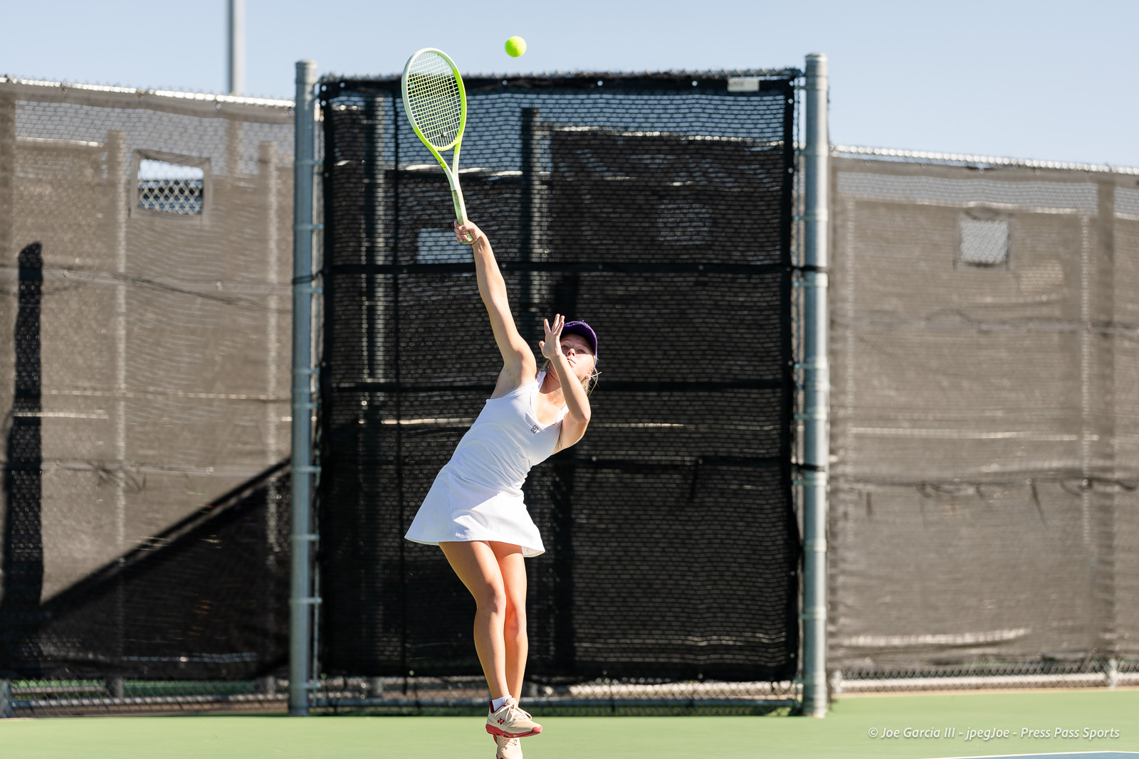 canyon-regional-tennis-36 | Press Pass Sports Female tennis player in white dress serving on an outdoor hard court, racket raised as ball rises above her