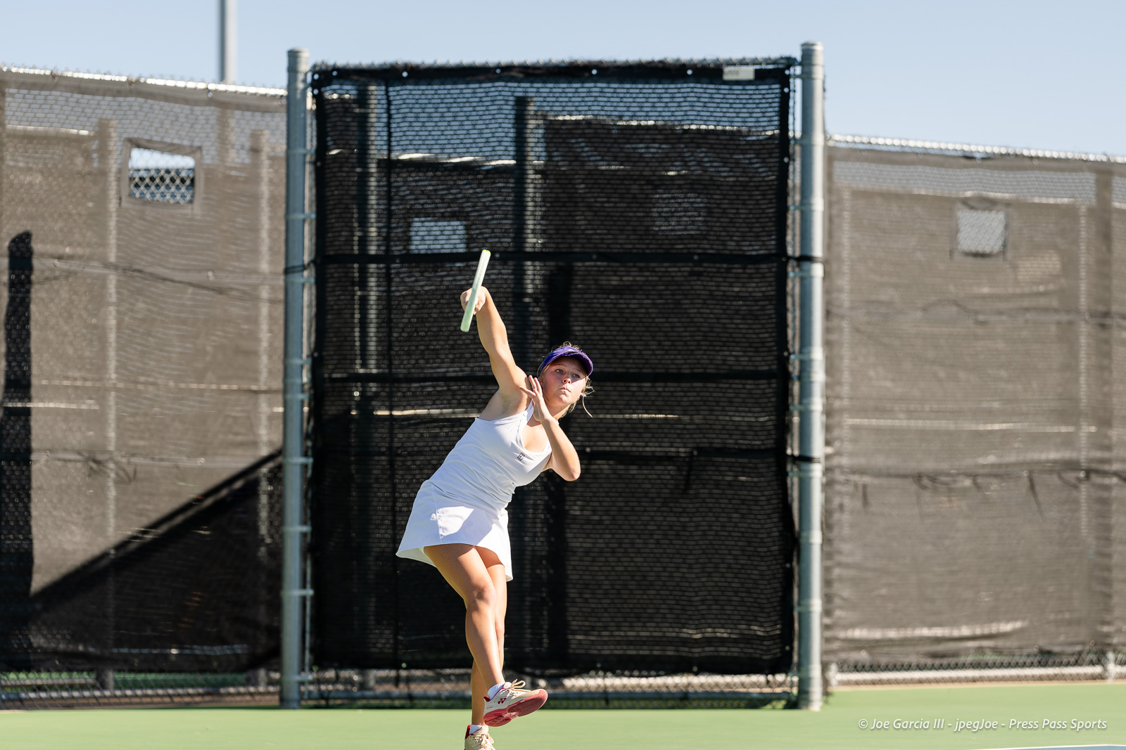 canyon-regional-tennis-37 | Press Pass Sports Female tennis player in a white outfit mid-serve on an outdoor court, racket raised high above her head on a sunny day.