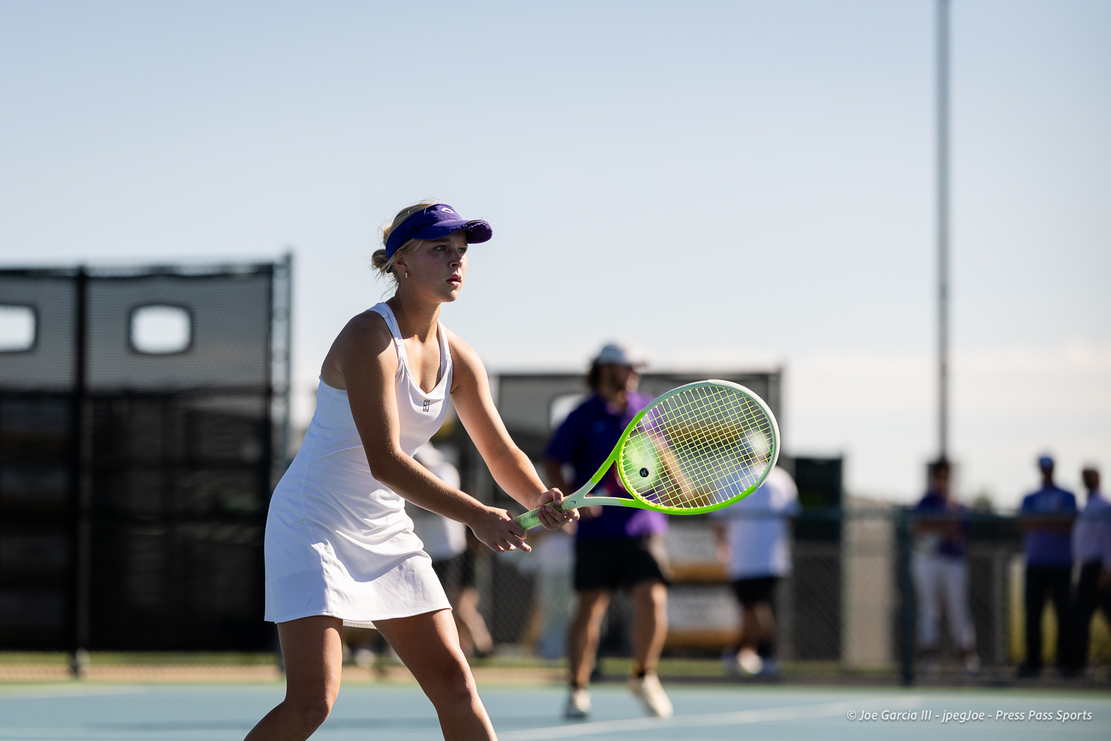 canyon-regional-tennis-39 | Press Pass Sports Female tennis player in a white outfit prepares to return a shot on an outdoor blue court, holding a neon-green racket.