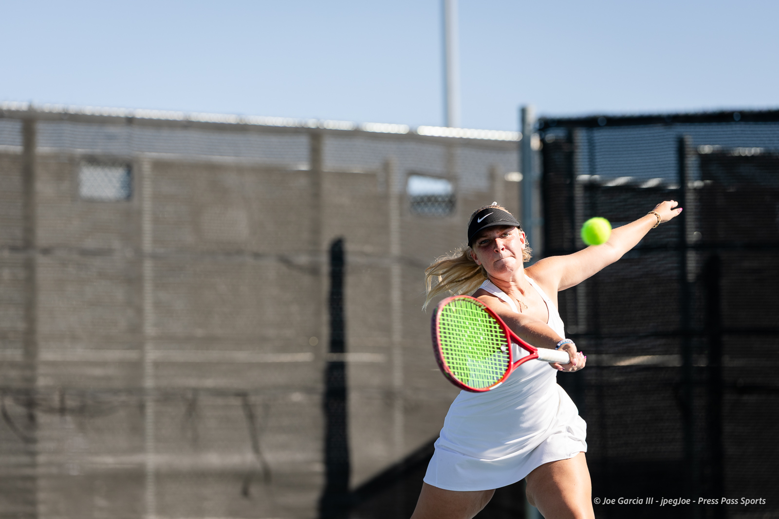 canyon-regional-tennis-40 | Press Pass Sports Female tennis player in a white dress and visor lunges to hit a forehand on an outdoor court as a ball approaches.