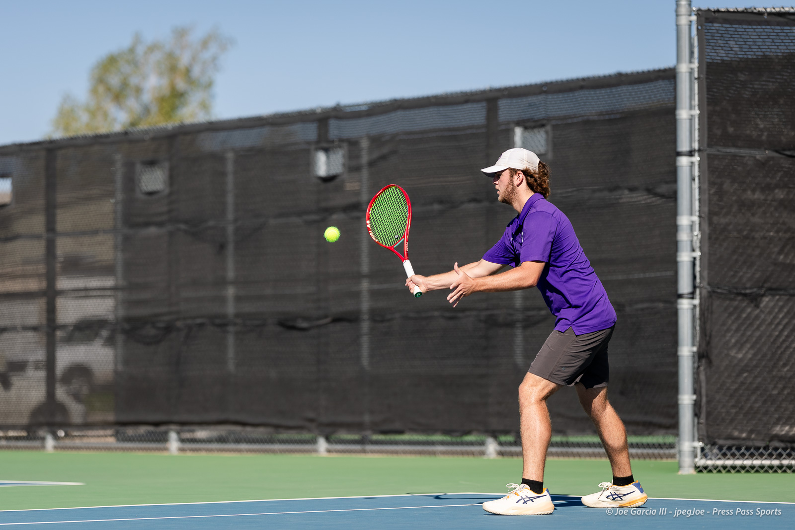 canyon-regional-tennis-44 | Press Pass Sports Tennis player in a purple shirt and white cap returns a forehand on a blue outdoor court.