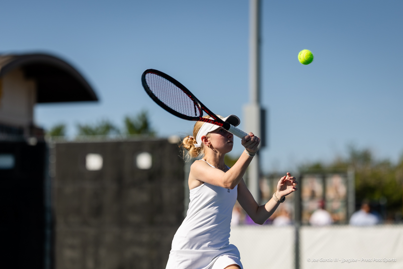 canyon-regional-tennis-47 | Press Pass Sports Female tennis player in white outfits swings racket to hit a bright tennis ball on an outdoor court under a clear blue sky.