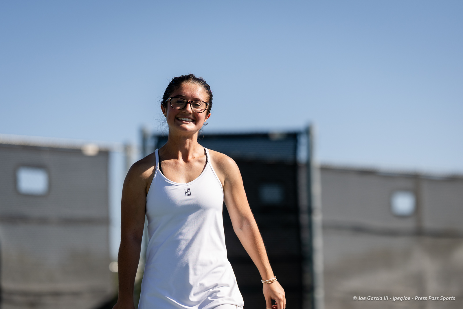 canyon-regional-tennis-61 | Press Pass Sports Smiling woman wearing a white tank top and glasses outdoors on a sunny day”,