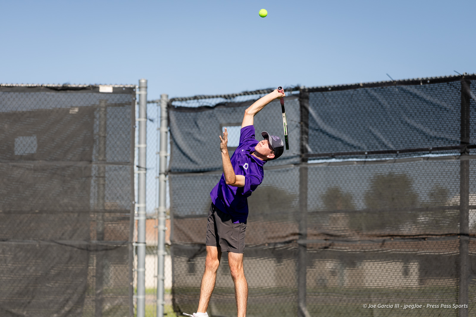 canyon-regional-tennis-63 | Press Pass Sports Male tennis player in a purple shirt serves the ball on an outdoor court, racket in motion and a bright tennis ball above him.