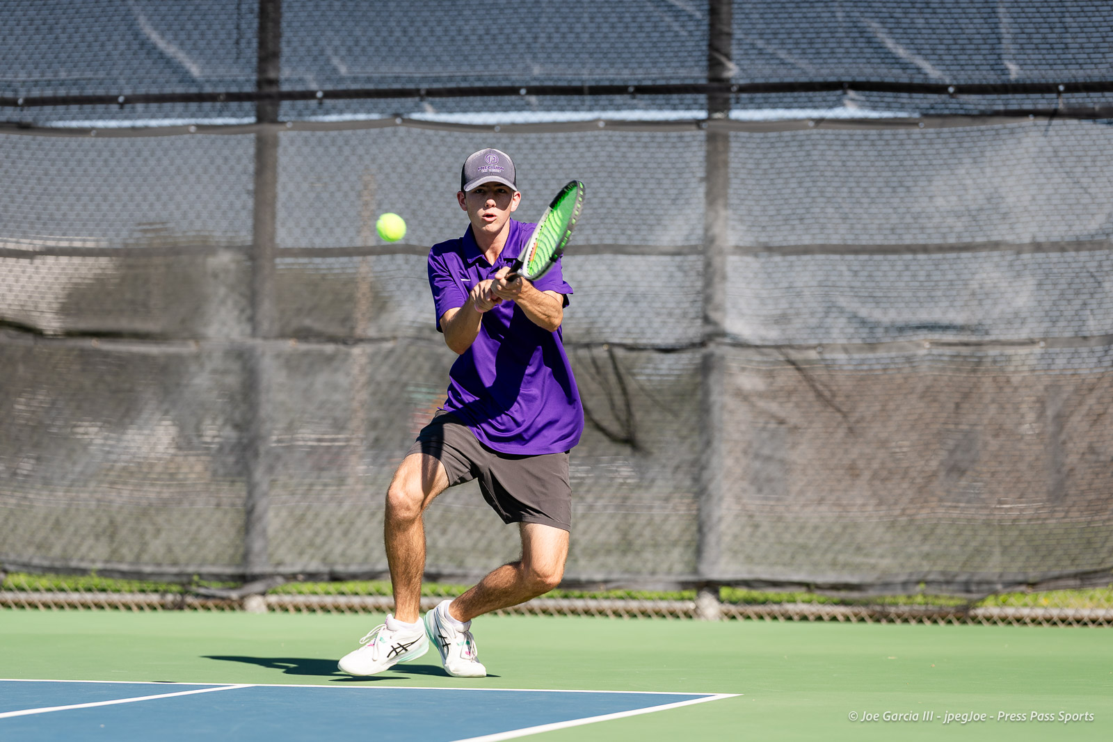 canyon-regional-tennis-71 | Press Pass Sports Tennis player in a purple shirt and cap prepares to hit a forehand on an outdoor court as a yellow ball approaches.