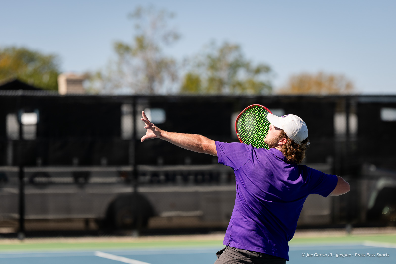 canyon-regional-tennis-76 | Press Pass Sports Tennis player in a purple shirt serves on a blue court, holding a green racket with a white cap.