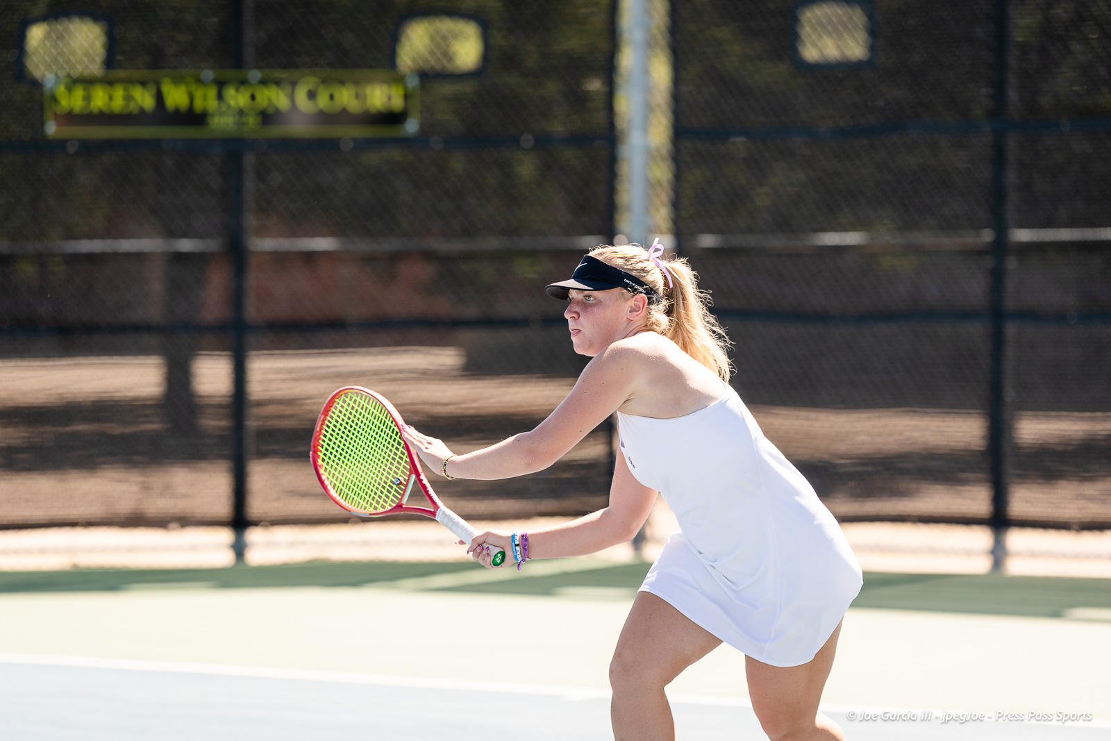 canyon-regional-tennis-78 | Press Pass Sports Female tennis player in a white outfit preparing a backhand on an outdoor court with a chain-link fence in the background.
