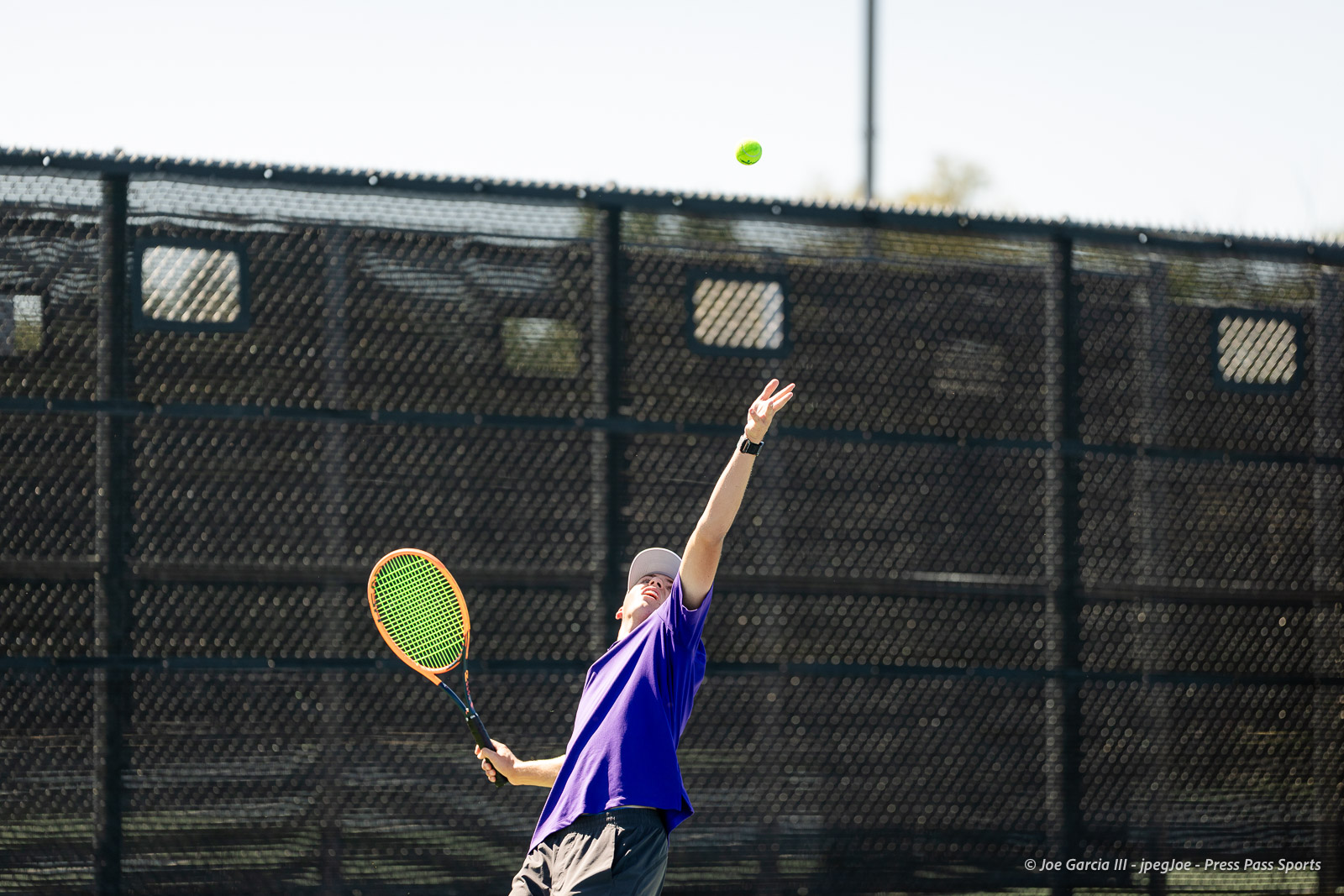 canyon-regional-tennis-87 | Press Pass Sports Tennis player in a purple shirt serves the ball on an outdoor court, racket raised with a neon orange frame.