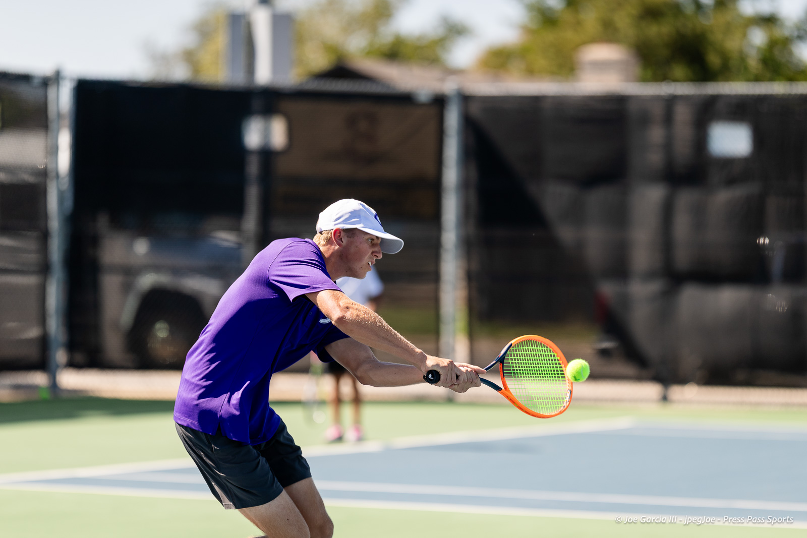 canyon-regional-tennis-92 | Press Pass Sports Tennis player in a purple shirt and white cap lunges to hit a bright yellow-green ball with an orange racket on a hard court.