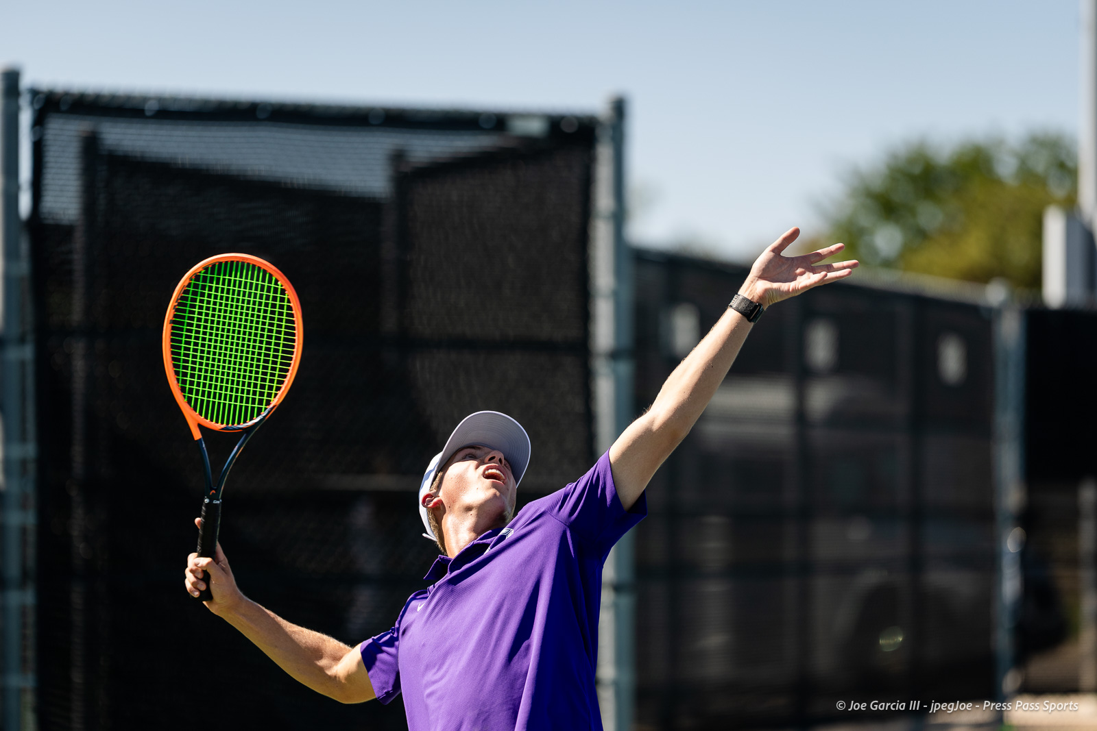canyon-regional-tennis-93 | Press Pass Sports Tennis player in a purple shirt and white cap serving with an orange-framed racket on an outdoor court.