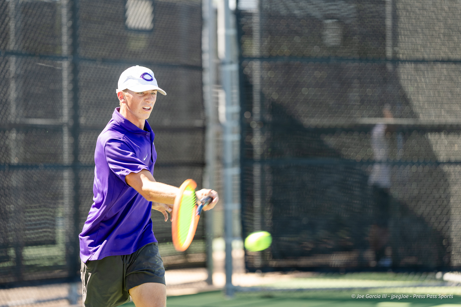 canyon-regional-tennis-94 | Press Pass Sports Male tennis player in a purple shirt and white cap hitting a forehand on an outdoor court