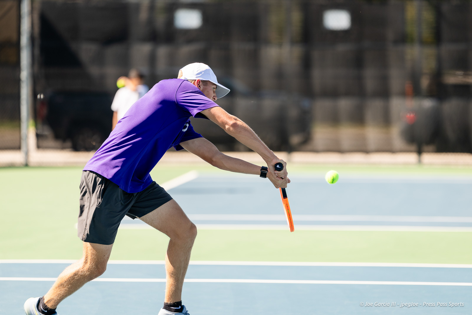 canyon-regional-tennis-96 | Press Pass Sports Tennis player in a purple shirt and white cap extending to hit a forehand on a blue hard court.