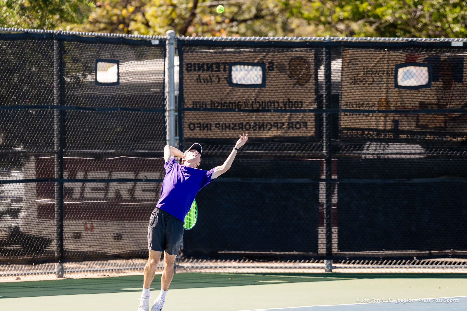 canyon-regional-tennis-97 | Press Pass Sports Tennis player in a purple shirt serves on an outdoor court, ball mid‑air above the racket in a sunny setting.