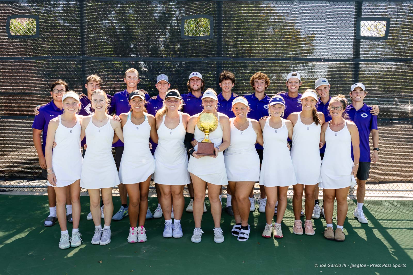 canyon-regional-tennis-107 | Press Pass Sports Tennis team posing on the court with a gold trophy; front row in white dresses, back row in purple uniforms.