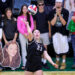 IMG_1378 | Press Pass Sports Female volleyball player in black spikes the ball as a crowd watches from the stands behind her, including cutout banner faces at the bottom edge.