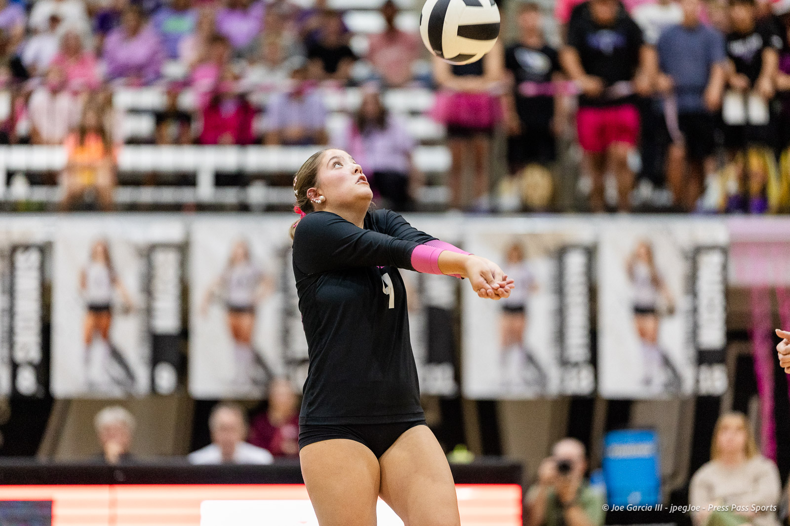 canyon-vs-west-plains-2026-2 | Press Pass Sports Female volleyball player in black uniform serving the ball during a match in a crowded gymnasium with spectators watching.