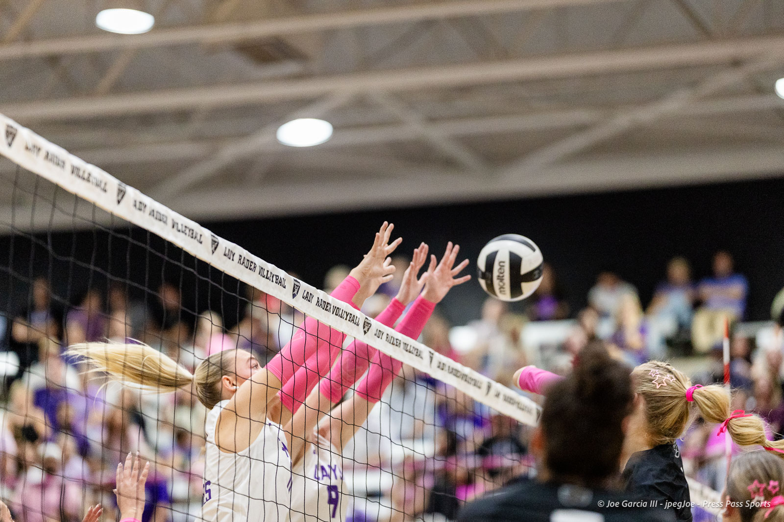 canyon-vs-west-plains-2026-4 | Press Pass Sports Volleyball players reach over the net to block a ball as spectators watch from the stands.