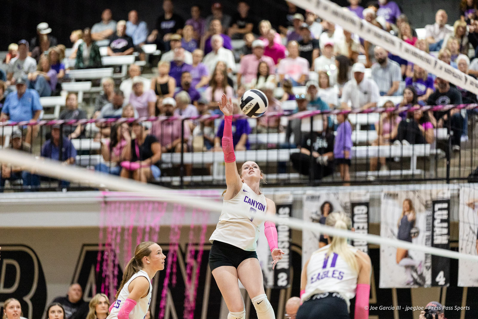 canyon-vs-west-plains-2026-5 | Press Pass Sports Canyon volleyball player in white jersey (no. 9) leaps to spike the ball mid-air as a crowded gym watches from the stands behind.