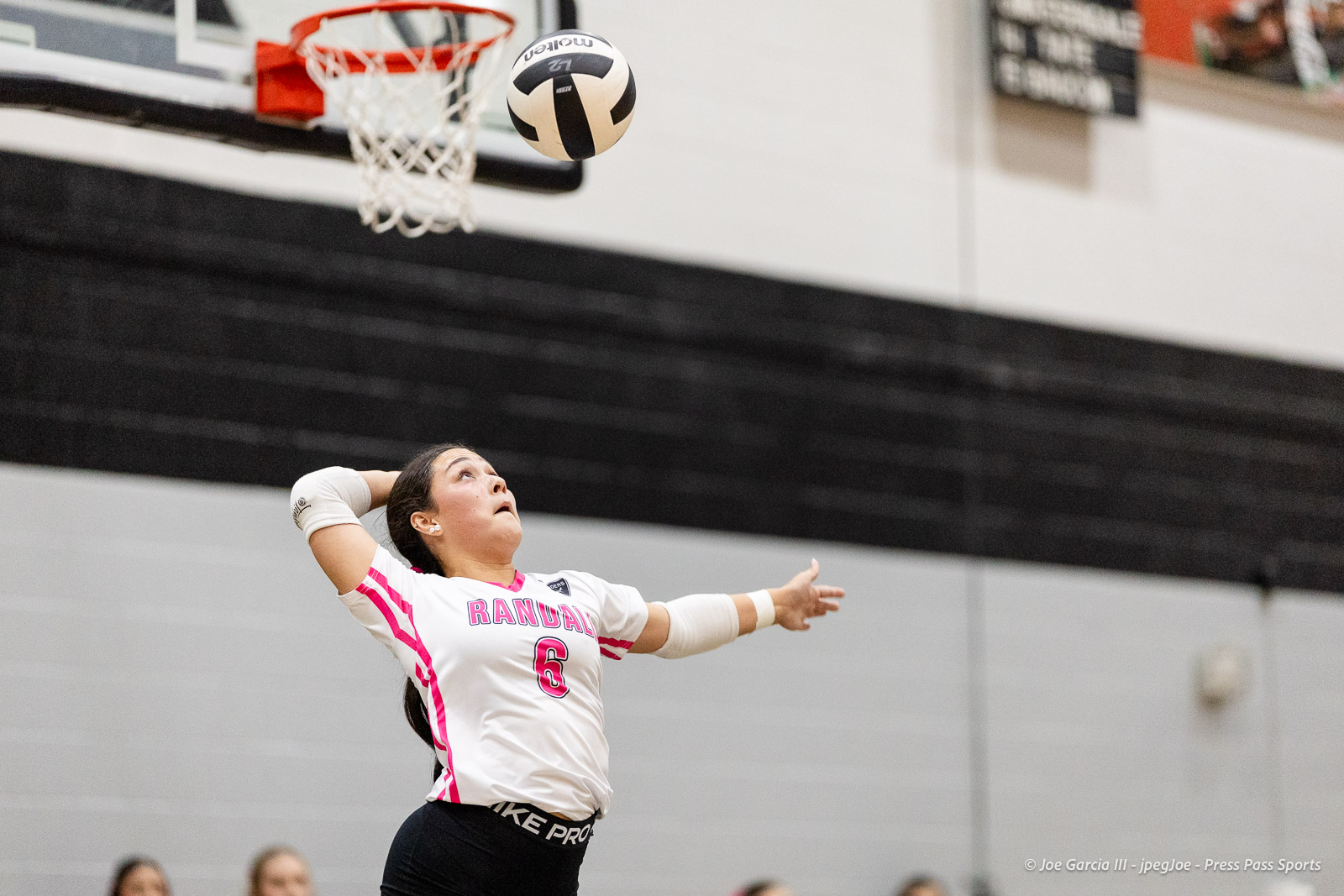 canyon-vs-west-plains-2026-9 | Press Pass Sports Female volleyball player in a white and pink jersey (number 6) leaps and hits the ball toward the hoop in a gym.
