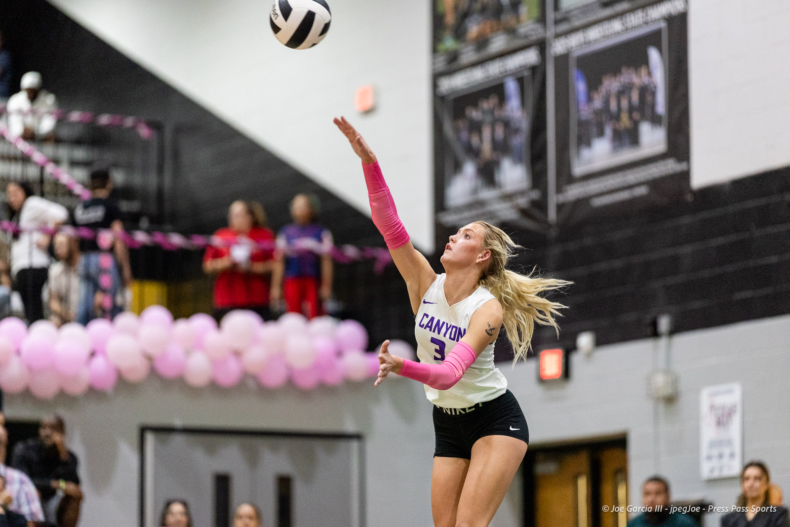 canyon-vs-west-plains-2026-11 | Press Pass Sports Volleyball player in a Canyon jersey (#3) spikes the ball in a gym with pink balloons lining the stands behind her.