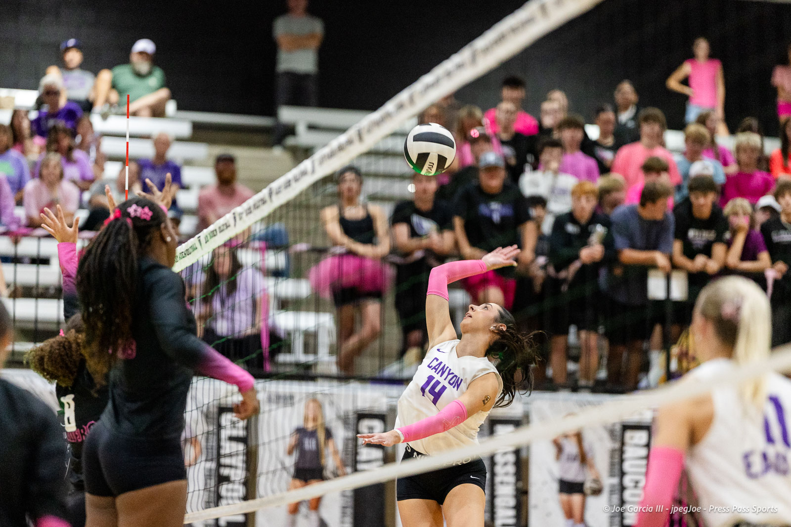 canyon-vs-west-plains-2026-21 | Press Pass Sports Volleyball player in white Canyon jersey spikes the ball at the net as a crowd watches from the bleachers.